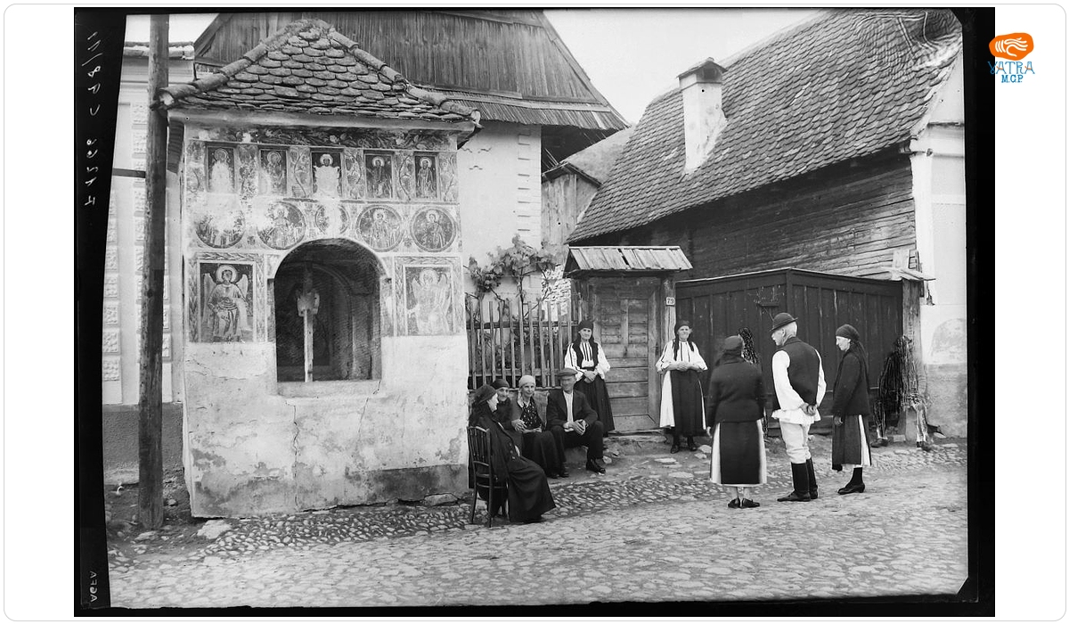 Grup de țărani pe ulița satului, lângă troiță